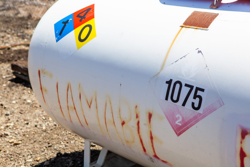 Close-up of a rusted white propane tank with hazardous material labels, including a red flammable gas symbol marked with the number 1075