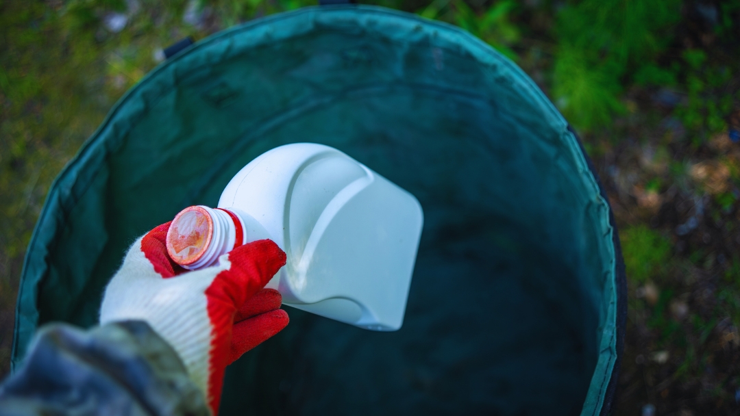 How to dispose of antifreeze safely and legally: person wearing protective gloves properly disposing of antifreeze container in designated waste receptacle