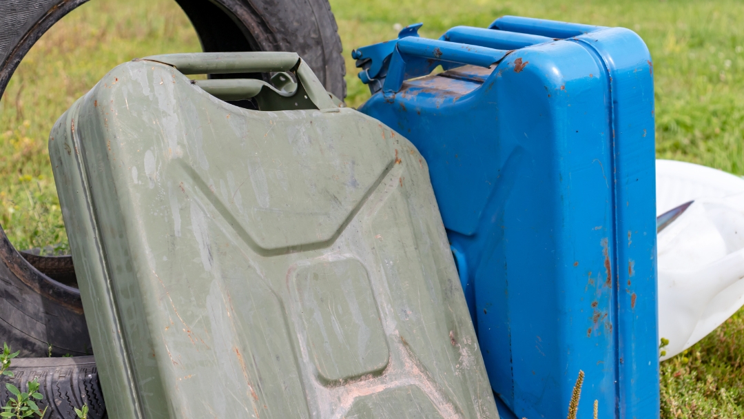 Old green and blue jerry cans on grass, representing how to dispose of old gas safely following industrial safety and compliance guidelines.